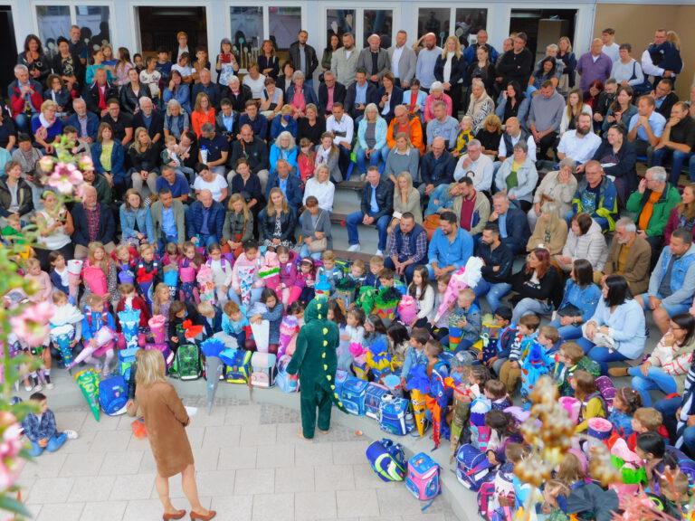 Im Atrium sitzen viele Kinder und Eltern und vorne steht ein verkleideter Drache